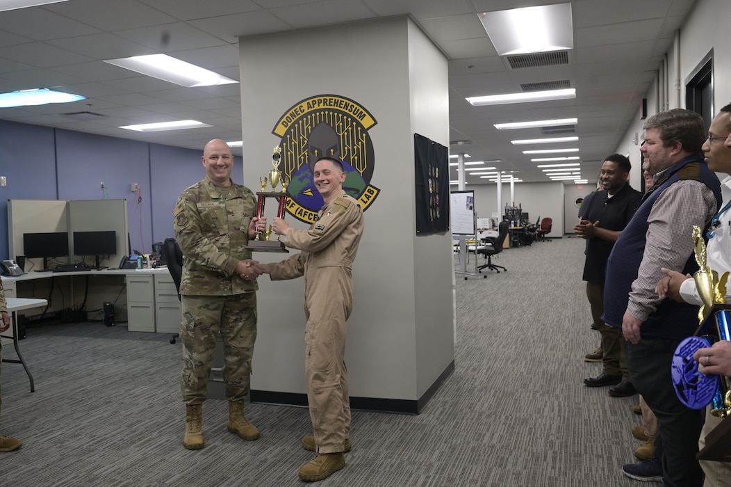 Col. Matthew Reilman, 9th Air Force chief of staff, presents a trophy to Capt. Daniel Taylor, 9th Air Force (Air Forces Central) A3, bed-down coordinator, during the Command Technology and Data Office (CTDO) Battle Lab Hack-a-thon event, May 3, 2024, at Shaw Air Force Base, S.C. The AFCENT ‘Battle Lab’ premiered a data centric, week-long event focused on warfighting solutions for problem sets within the CENTCOM area of responsibility. The teams were ranked by a panel of judges for their efforts to analyze data and provide solutions with real world applications.  (U.S. Air Force photo Staff Sgt. Adriana Barrientos)