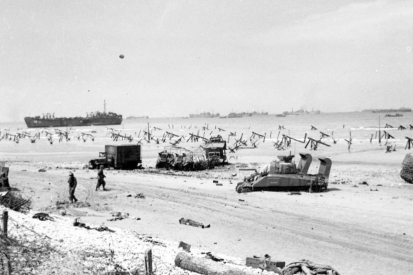 A black and white photo shows military gear and people on a beach.