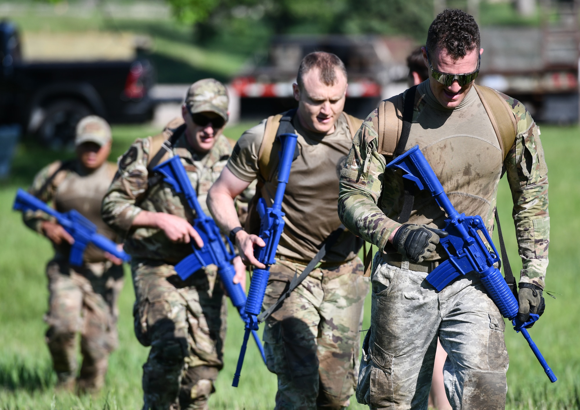 four military members walk in a single file line carrying riffles
