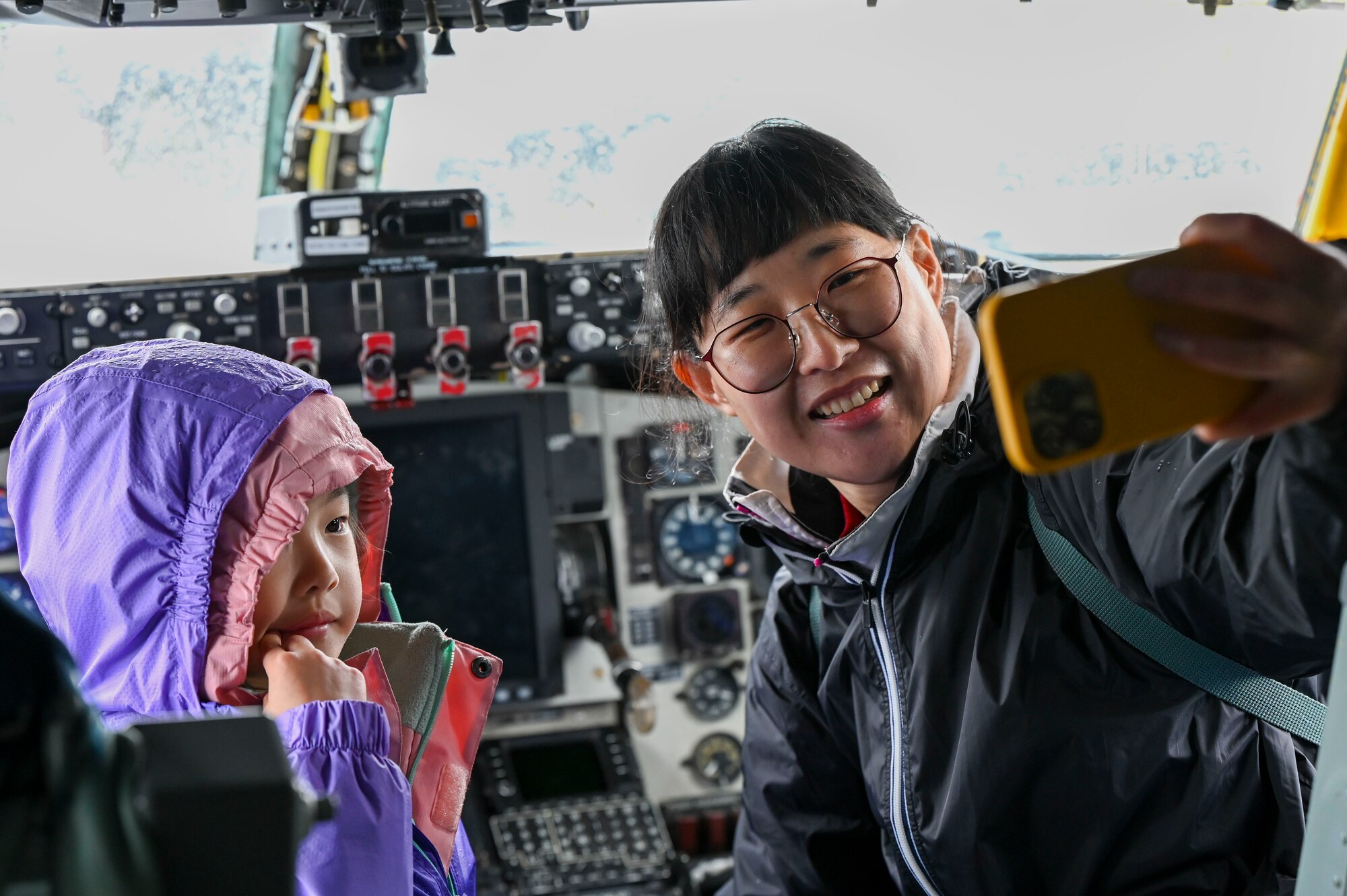 A woman takes a photo with her daughter in the cockpit of a jet.