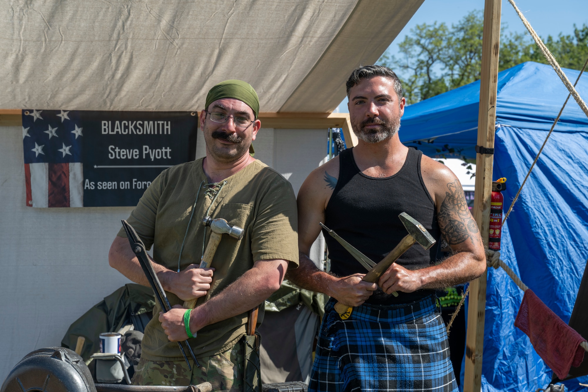 Two men pose for a picture with their blacksmithing tools.