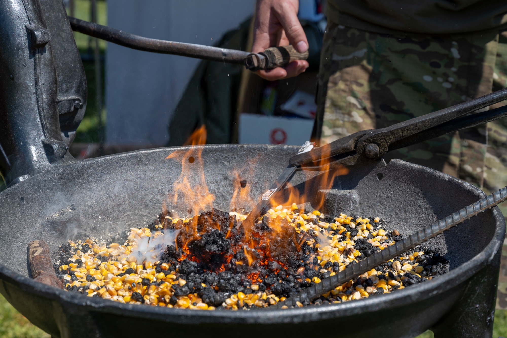 A man heats up a piece of metal in a forge filled with burning corn.