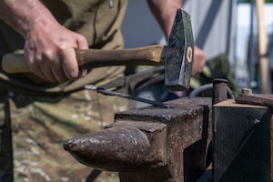 A man hammers a piece of metal on an anvil.