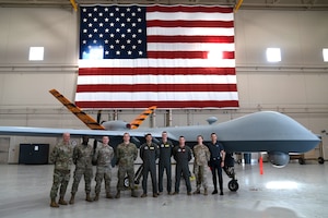 A group of military members in uniform pose for the camera in front of a remotely piloted aircraft.