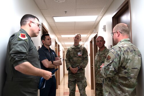 Five men, four of them in military uniforms, stand talking in a hallway.