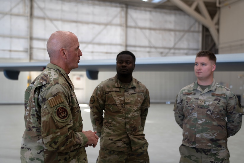 An airman speaks to two other airmen in a hangar-type area.
