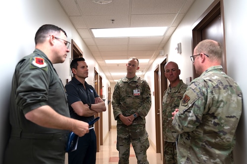 Five men, four of them in military uniforms, stand talking in a hallway.