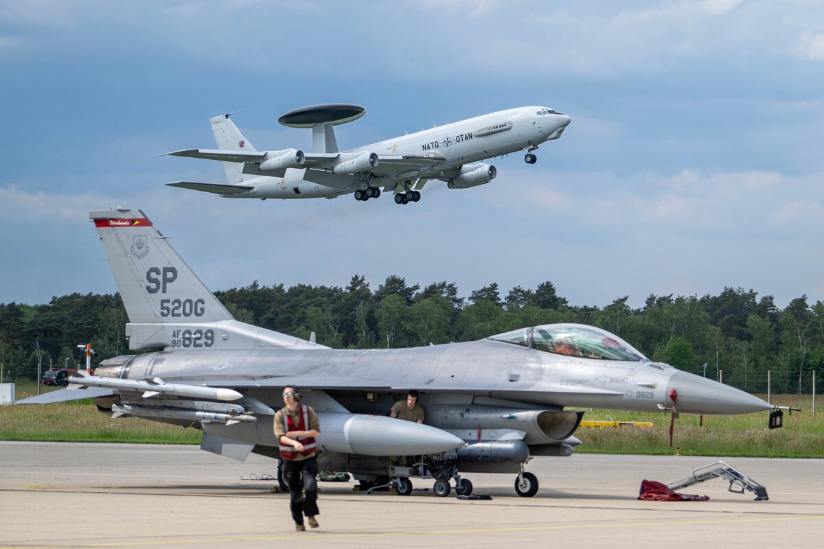 A plane flies in air while another plane sits on ground.