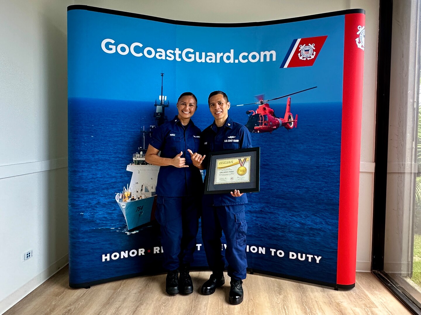 Chief Petty Officer Deren Perez, a figure of inspiration and leadership within the U.S. Coast Guard, stands with his spouse, Petty Officer 3rd Class Triana Perez, after being presented with the U.S. Coast Guard's Elite Male Athlete of the Year award at the newly relocated recruiting office in Tamuning, Guam, on May 17, 2024. The award, presented on behalf of the U.S. Coast Guard MWR and the Community Services Command, is a testament to his exceptional athletic abilities and his unwavering dedication to his community. (U.S. Coast Guard photo by Chief Warrant Officer Sara Muir)