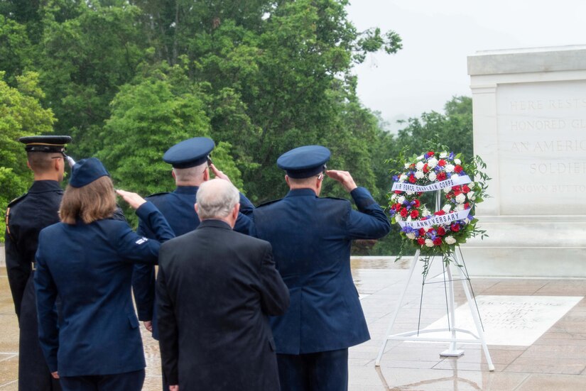 Uniformed service members and a person in a business suit salute a wreath at Arlington National Cemetery.