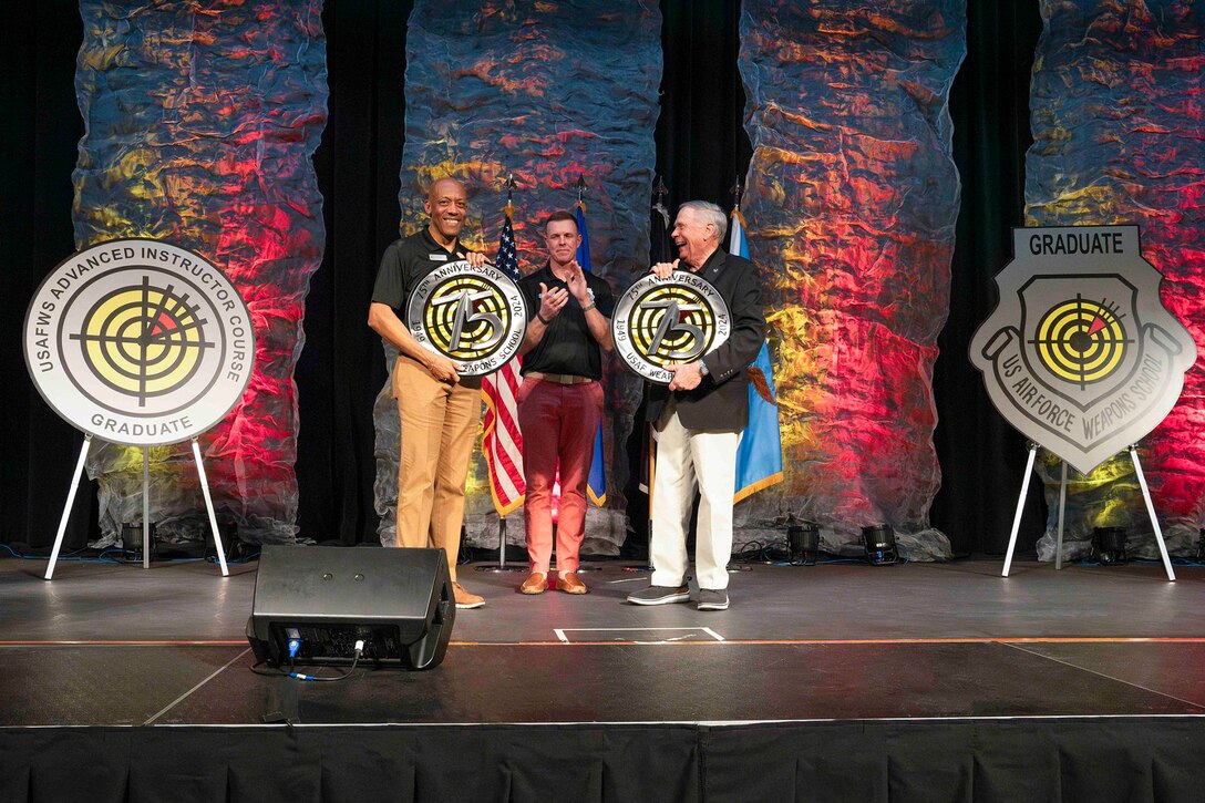 Air Force Gen. CQ Brown, Jr., holds a large disc on a stage while another person in civilian dress does the same and a third applauds.
