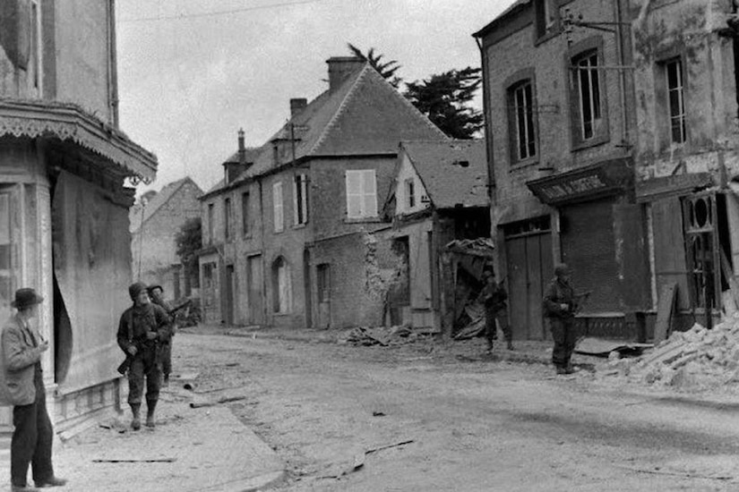 Soldiers with guns walk down a street.