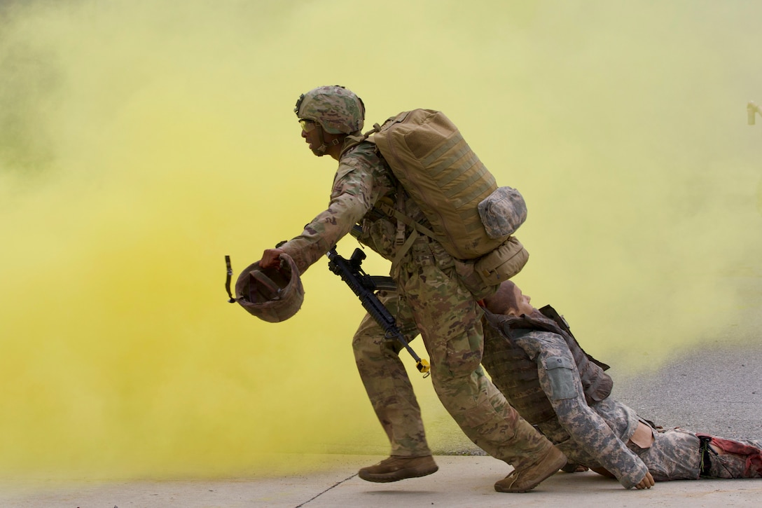 A soldier carrying a weapon and backpack pulls a dummy in uniform through clouds of yellow smoke.