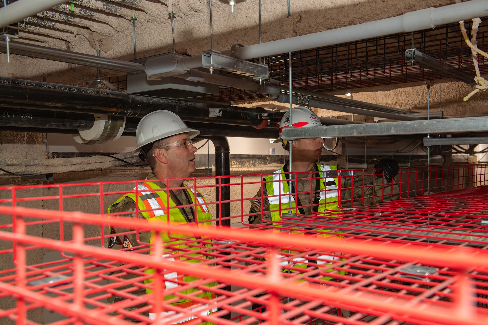 Two men in military uniforms wearing construction attire look at construction site