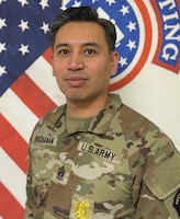 Male Soldier posing in front of the U.S. flag and the USAREC flag.