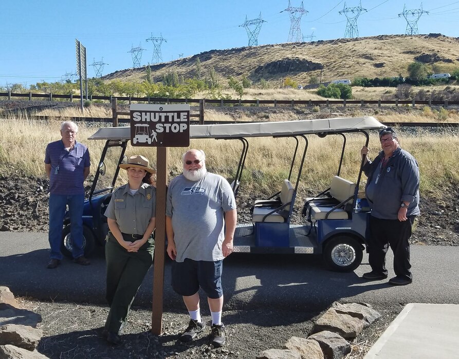 Park Ranger stands with three other volunteers and a golf cart in front of a grassy back drop.