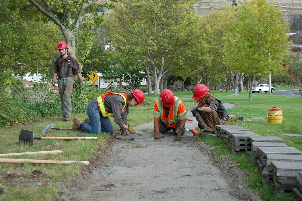 Four people outside clear a path to lay a sidewalk. All are wearing proper safety gear.