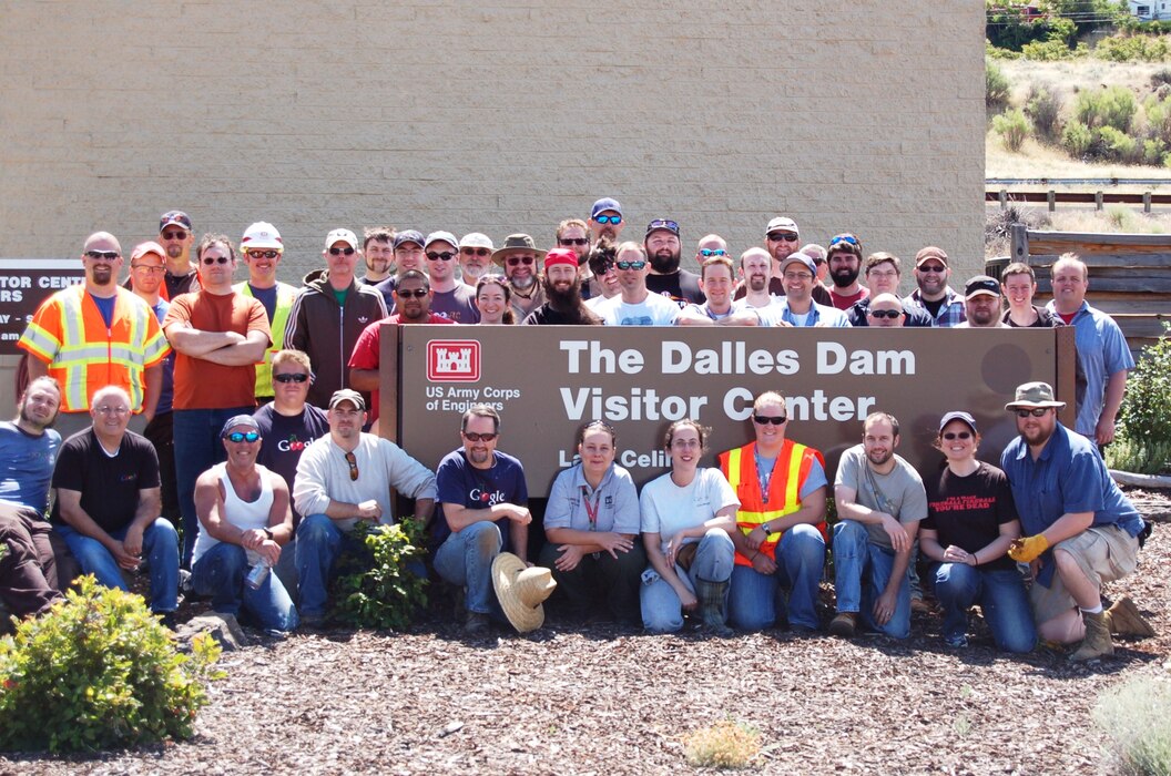 Several volunteers standing outside in front of a sign saying The Dalles Dam Visitor Center with the Corps of Engineers logo.