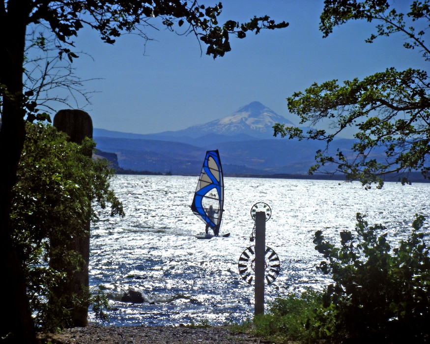 A kite surfer is on a body of water in front of a mountain backdrop.