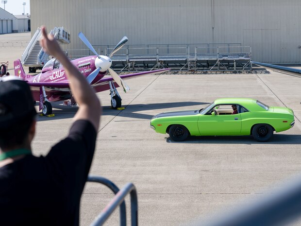 The driver of a green Dodge Challenger receives a signal that his photo was successfully taken by a volunteer photographer near a U-2 Dragon Lady during the Beale Auto Expo on May 18, 2024, at Beale Air Force Base, California.