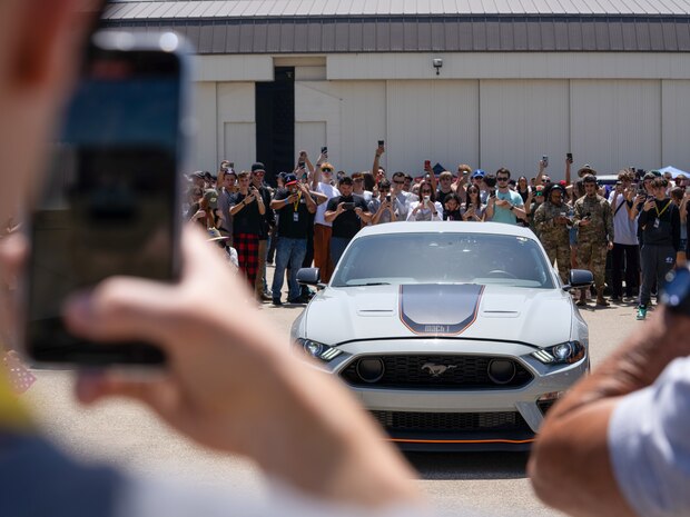 A crowd gathers to take pictures as a grey Ford Mustang revs its engine during the Loudest Car competition at the Beale Auto Expo, May 18, 2024, at Beale Air Force Base, California.