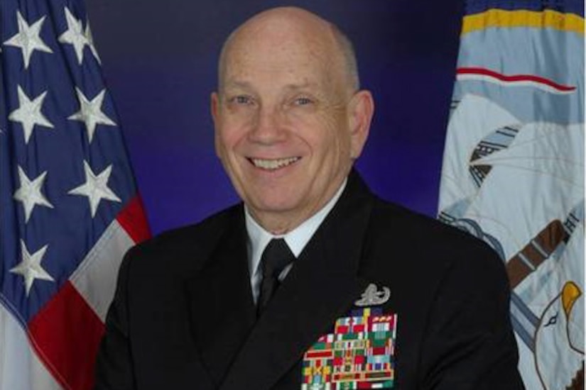 Portrait of Navy vice admiral seated in front of two flags