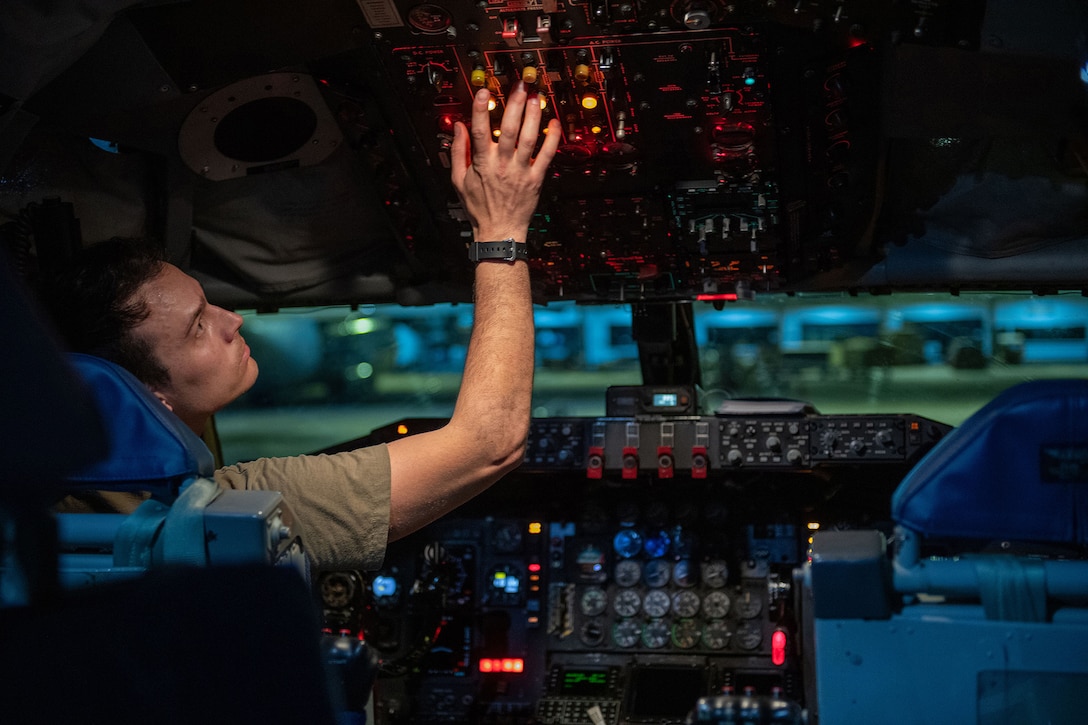 An airman presses buttons overhead while sitting in the cockpit of an aircraft.