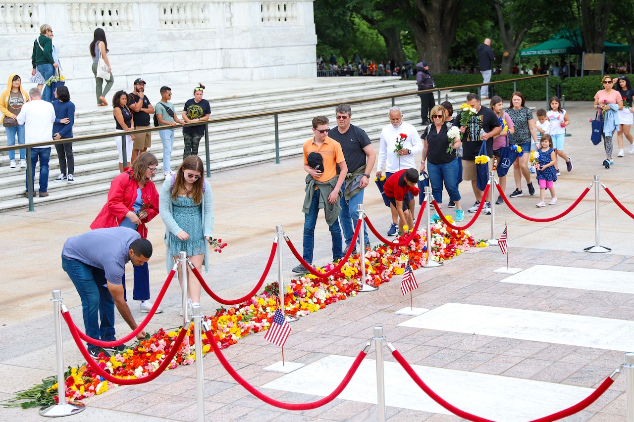 A line of people place flowers near a memorial.