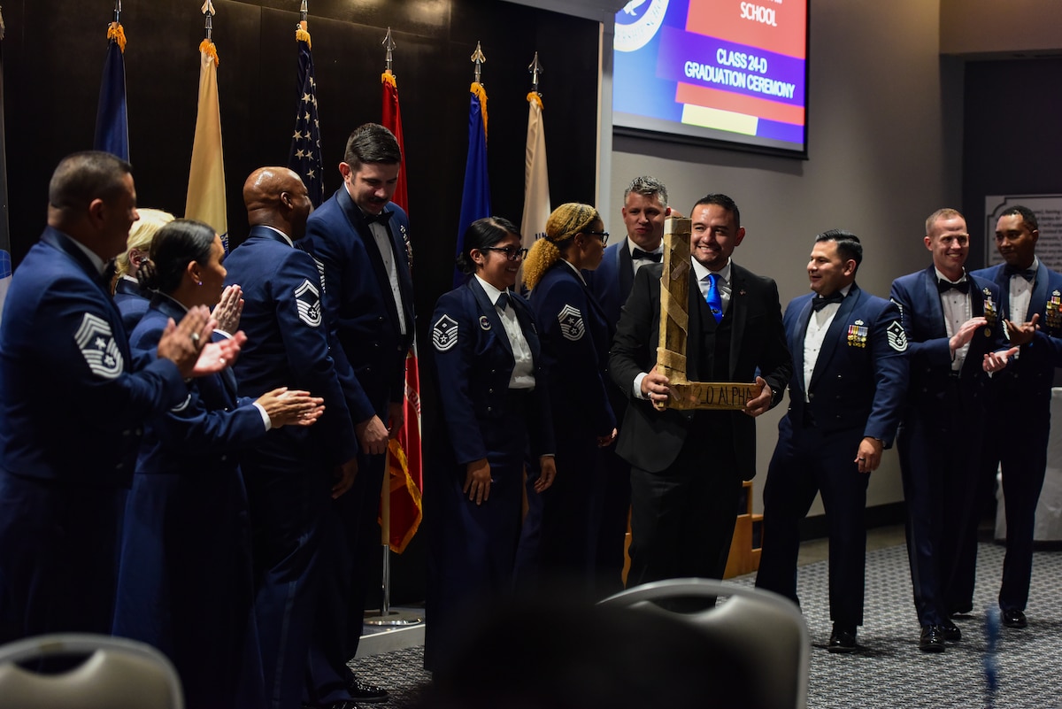 Emmanuel Lozano, Class 24-D Airman Leadership School graduate, receives the “L” from a group of first sergeants belonging to the 17th Training Wing during the Class 24-D ALS graduation at the Powell Event Center, Goodfellow Air Force Base, Texas, May 17, 2024. Every ALS class plays a volleyball game with the first sergeants and the winning team presents the “L” to the losing team at graduation. (U.S. Air Force photo by Airman 1st Class Zach Heimbuch)