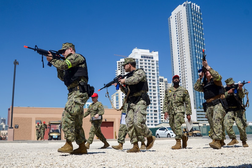 Service members in uniform carry rifles in an urban area.