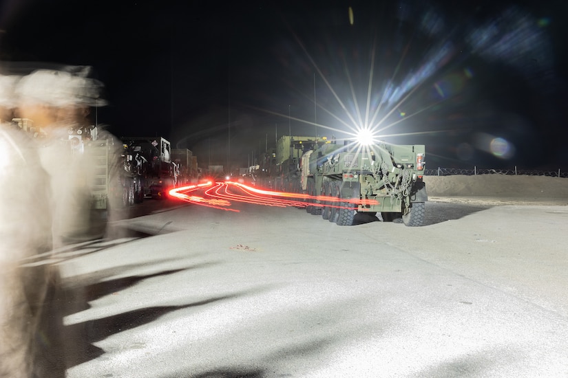 Combat vehicles move at night across pavement.