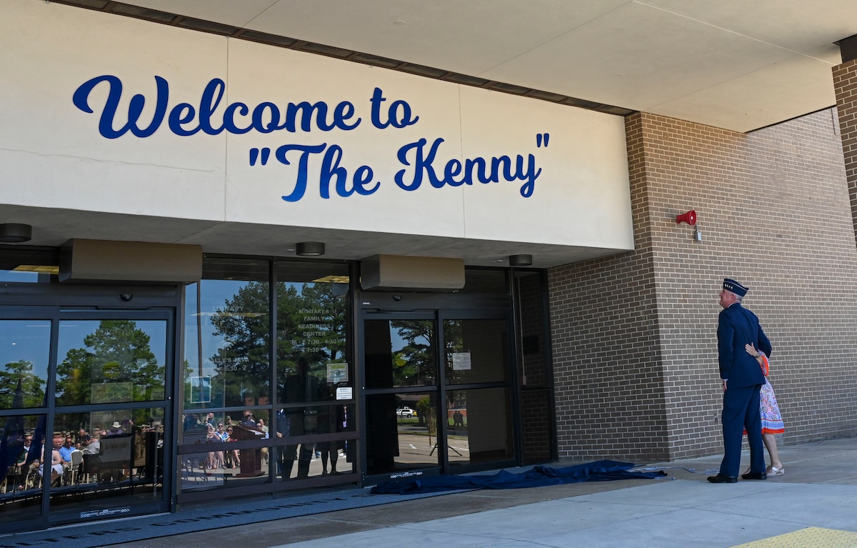 A General and person look at a sign stating 'Welcome to "The Kenny"'