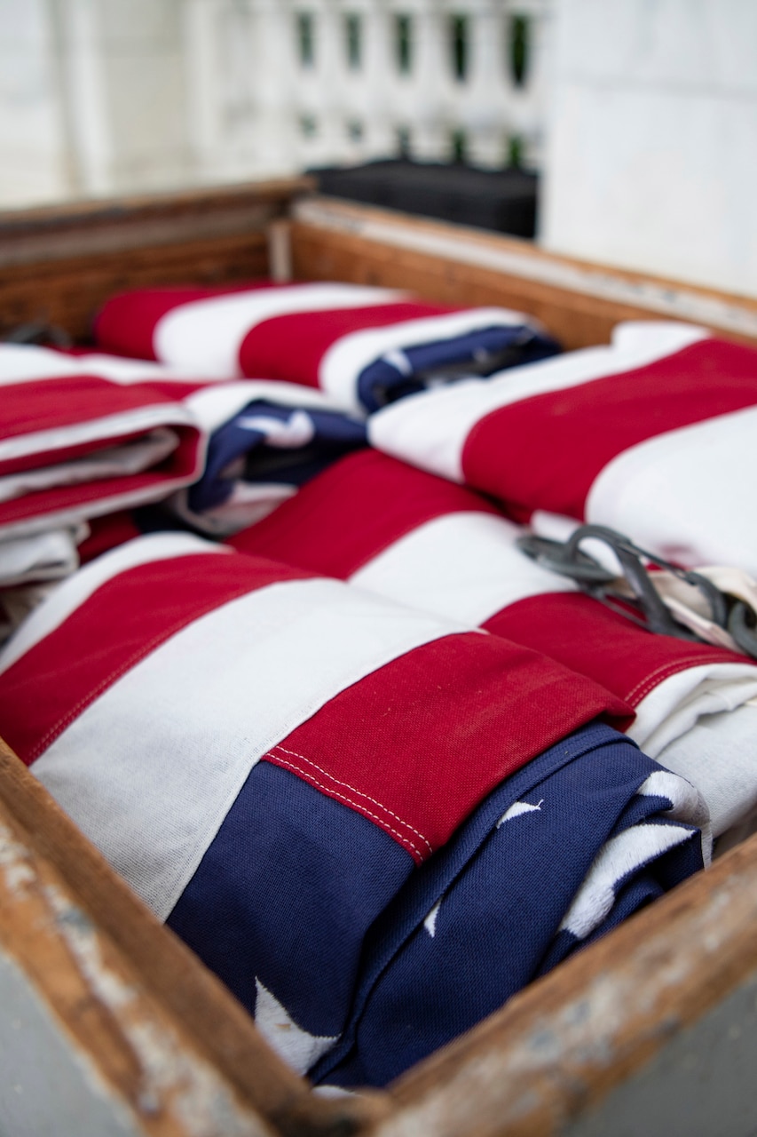 Folded U.S. flags sit in a rectangular wooden container outdoors.