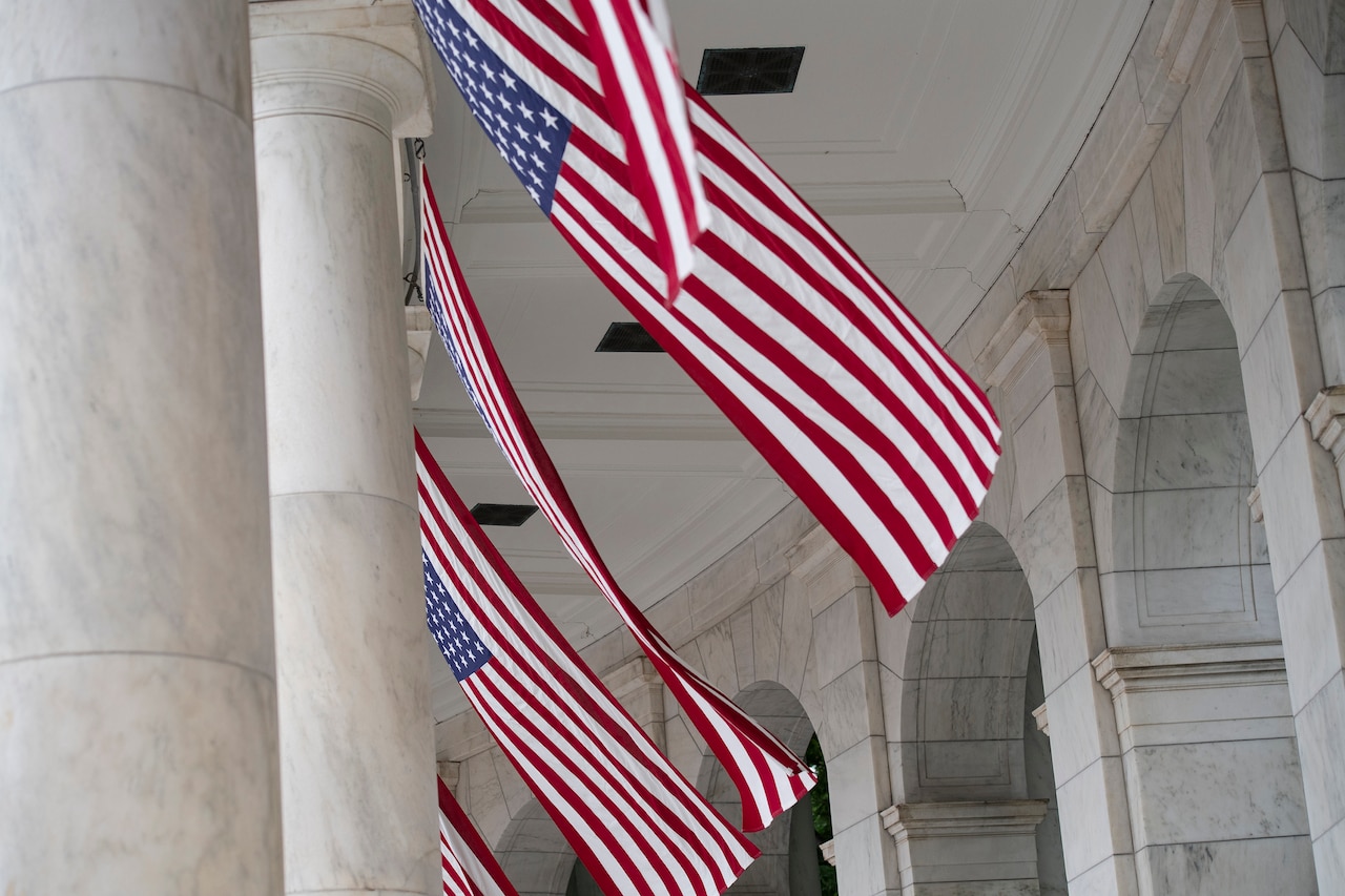 An employee hangs U.S. flags between white columns of an amphitheater.