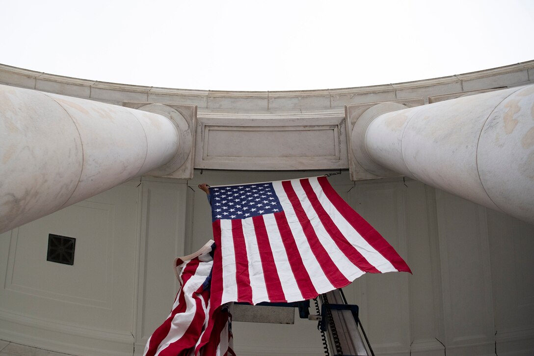 An employee hangs U.S. flags between white columns of an amphitheater.
