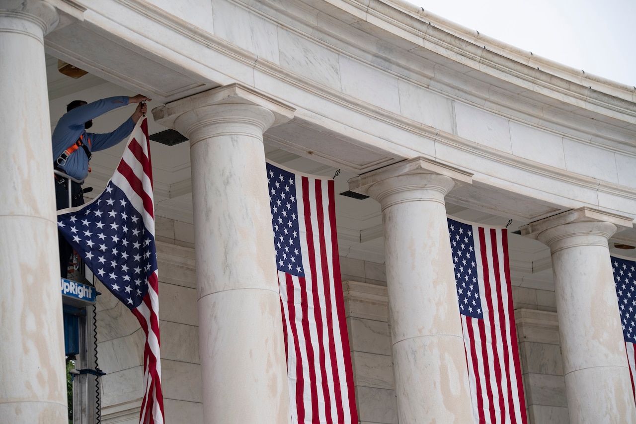 An employee hangs U.S. flags between white columns of an amphitheater.