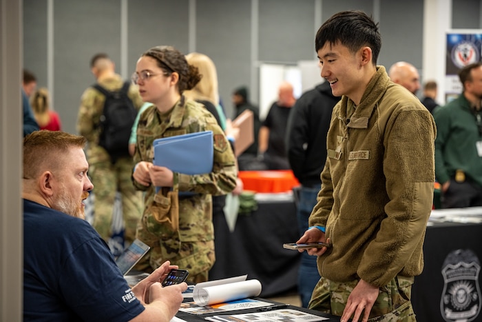 Two Airman standing in front of a job fair table talking with company recruiters.