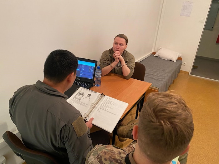 Airman sits at table with two other Airmen during simulated interrogation.