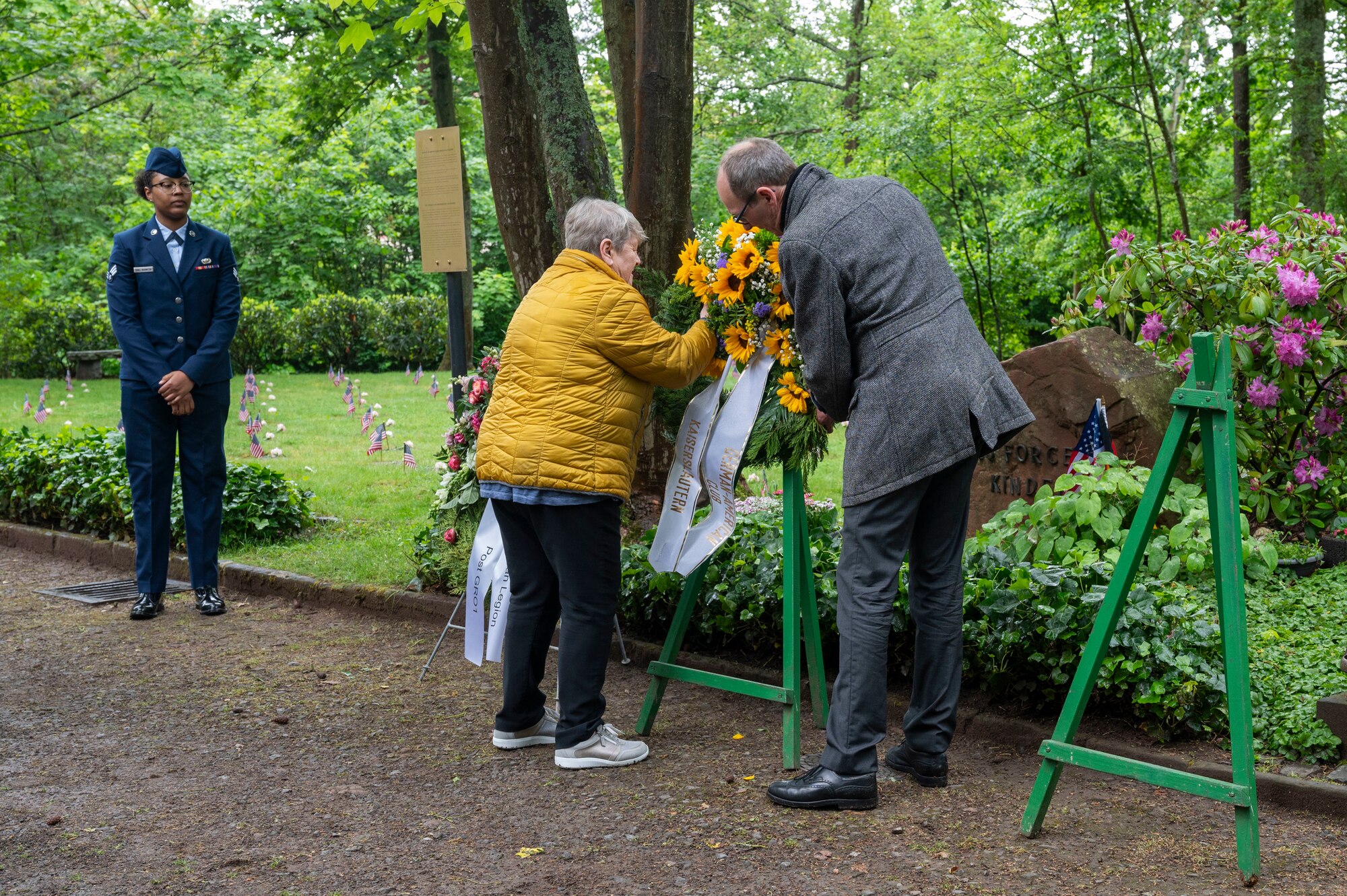 Two people place a wreath on a stand