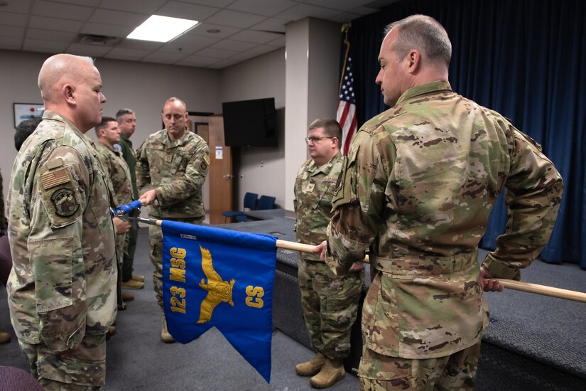 Lt. Col. Bryan Keating, right, 123rd Communications Squadron commander, unfurls the squadron’s new guidon as Chief Master Sgt. Brian Henry, superintendent, retires the unit’s previous colors during a ceremony at the Kentucky Air National Guard Base in Louisville, Ky., Feb. 11, 2024. The event marked the unit’s re-designation from flight to squadron. (U.S. Air National Guard photo by Staff Sgt. Chloe Ochs)