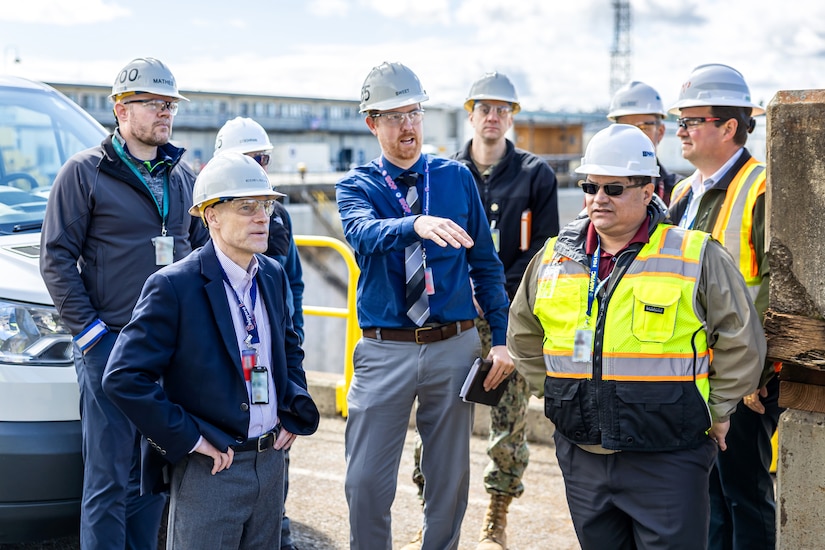 About eight people in hard hats look around at a dock.