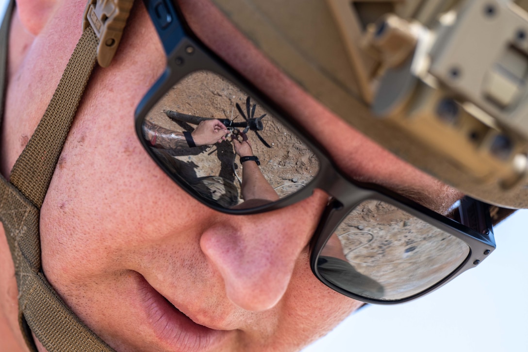 An airman's face focuses on a small device that is seen reflected in the airman’s sunglasses.