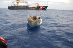 A migrant chug drifts in the waters after having its migrants onboard disembarked. The Coast Guard Cutter Willow sails in the background.