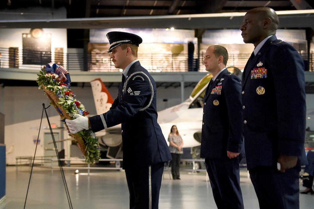 Three men in military uniform stand facing forward looking at a wreath being placed on an easel