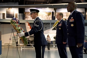 Three men in military uniform stand facing forward looking at a wreath being placed on an easel