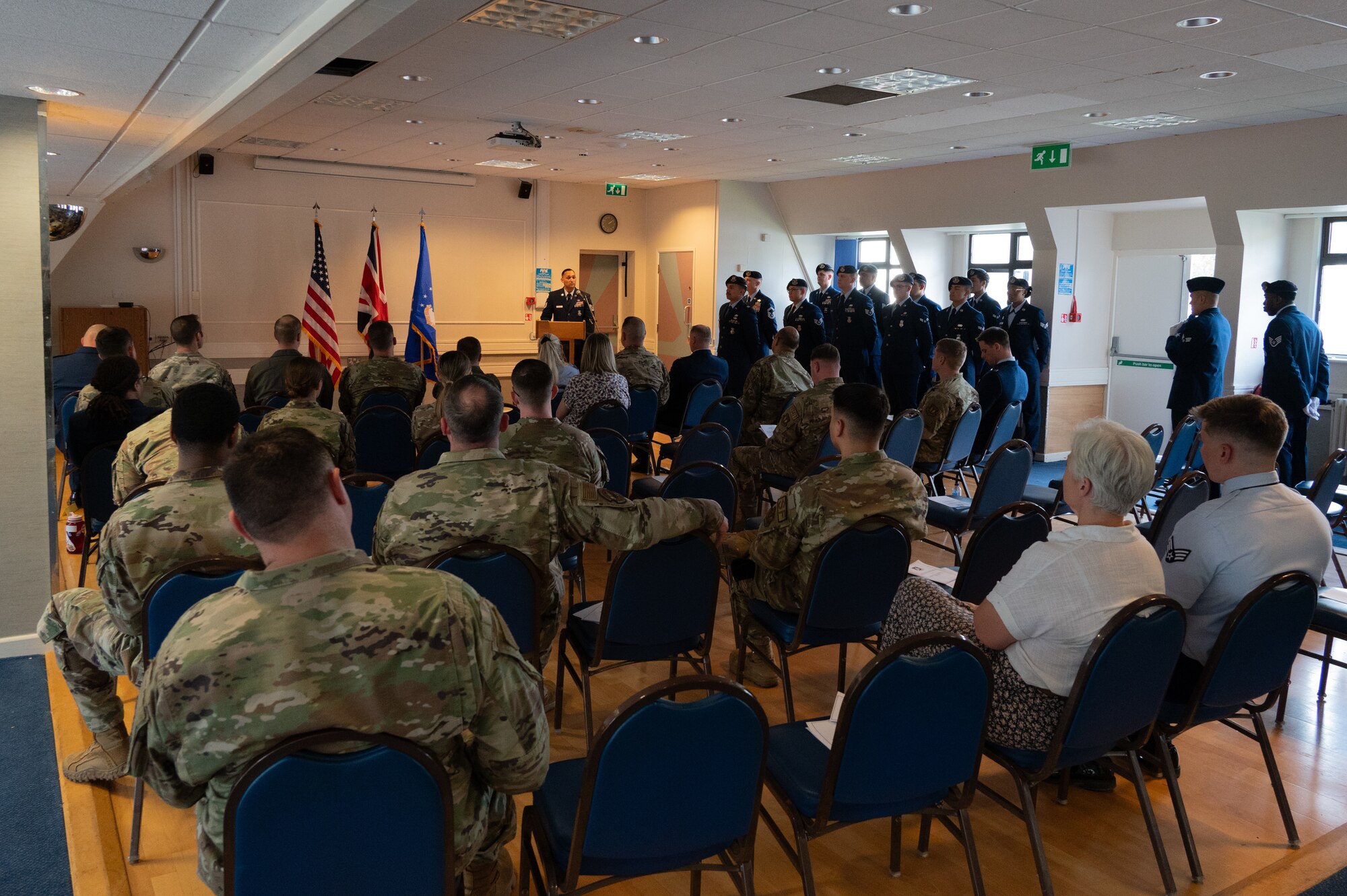 Civilians and Military members listen to a speech.