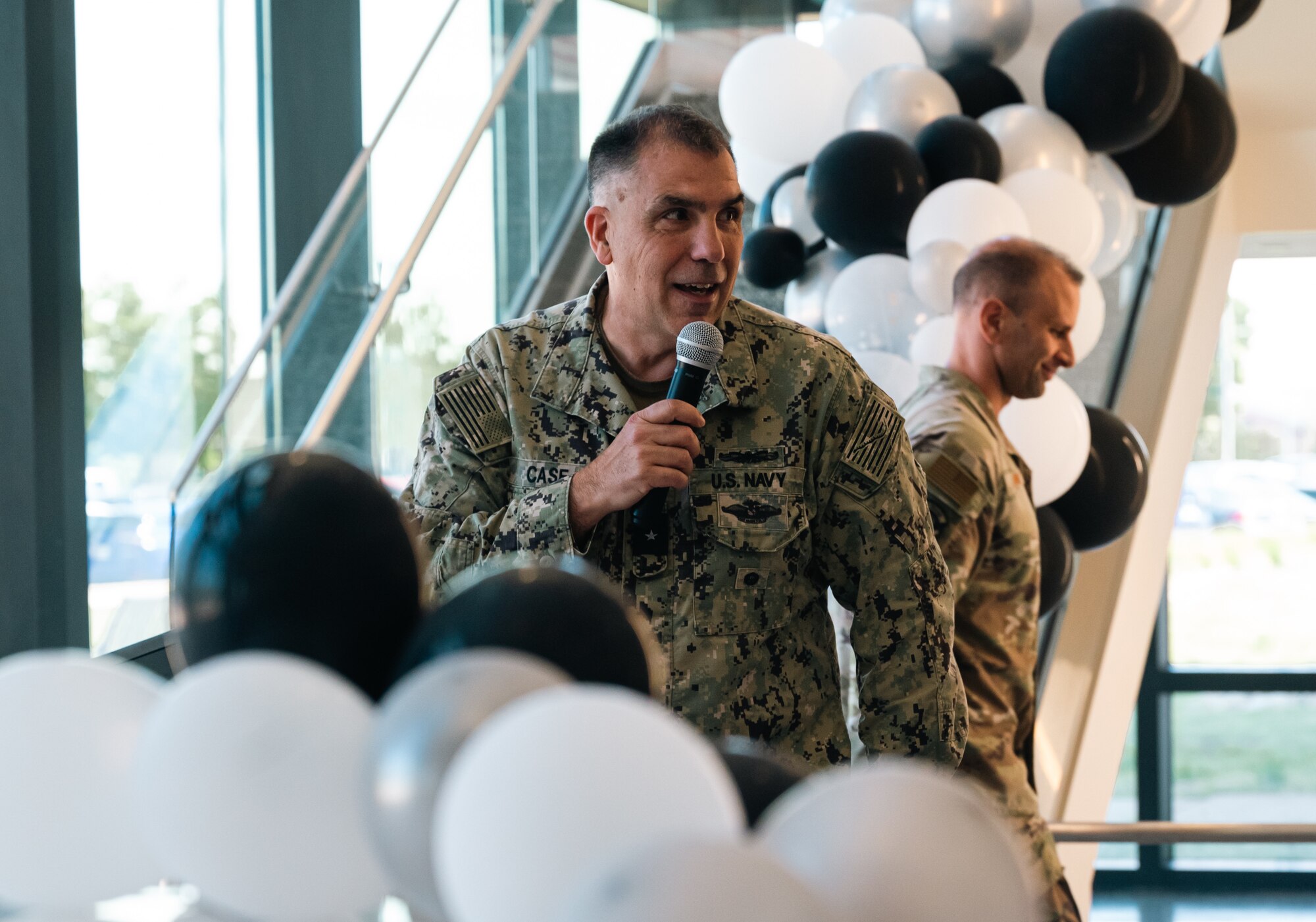 A navy man holds a mic surrounded by white and black balloons