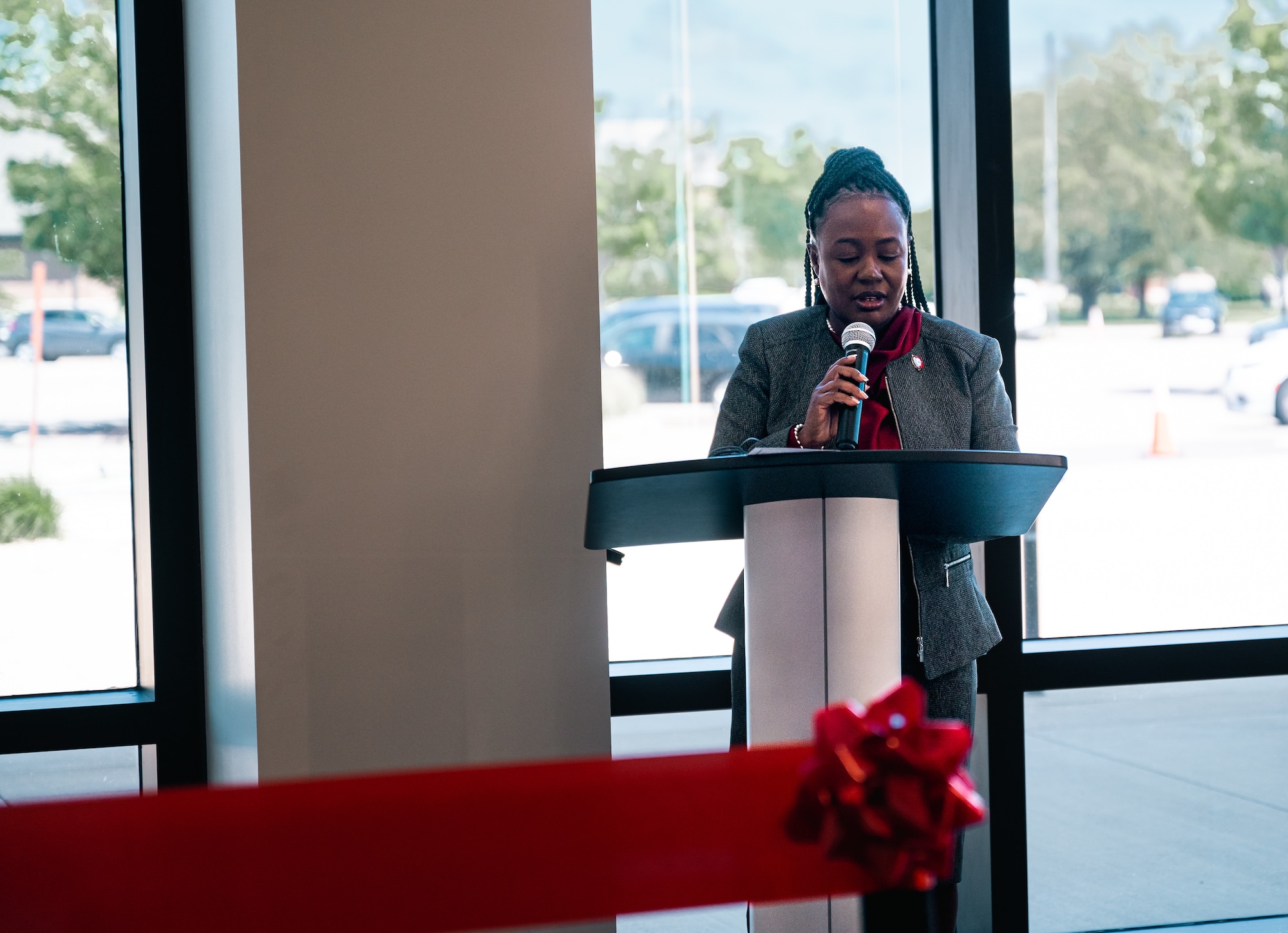 A women in a gray blazer and a red shirt holds a mic at a podium