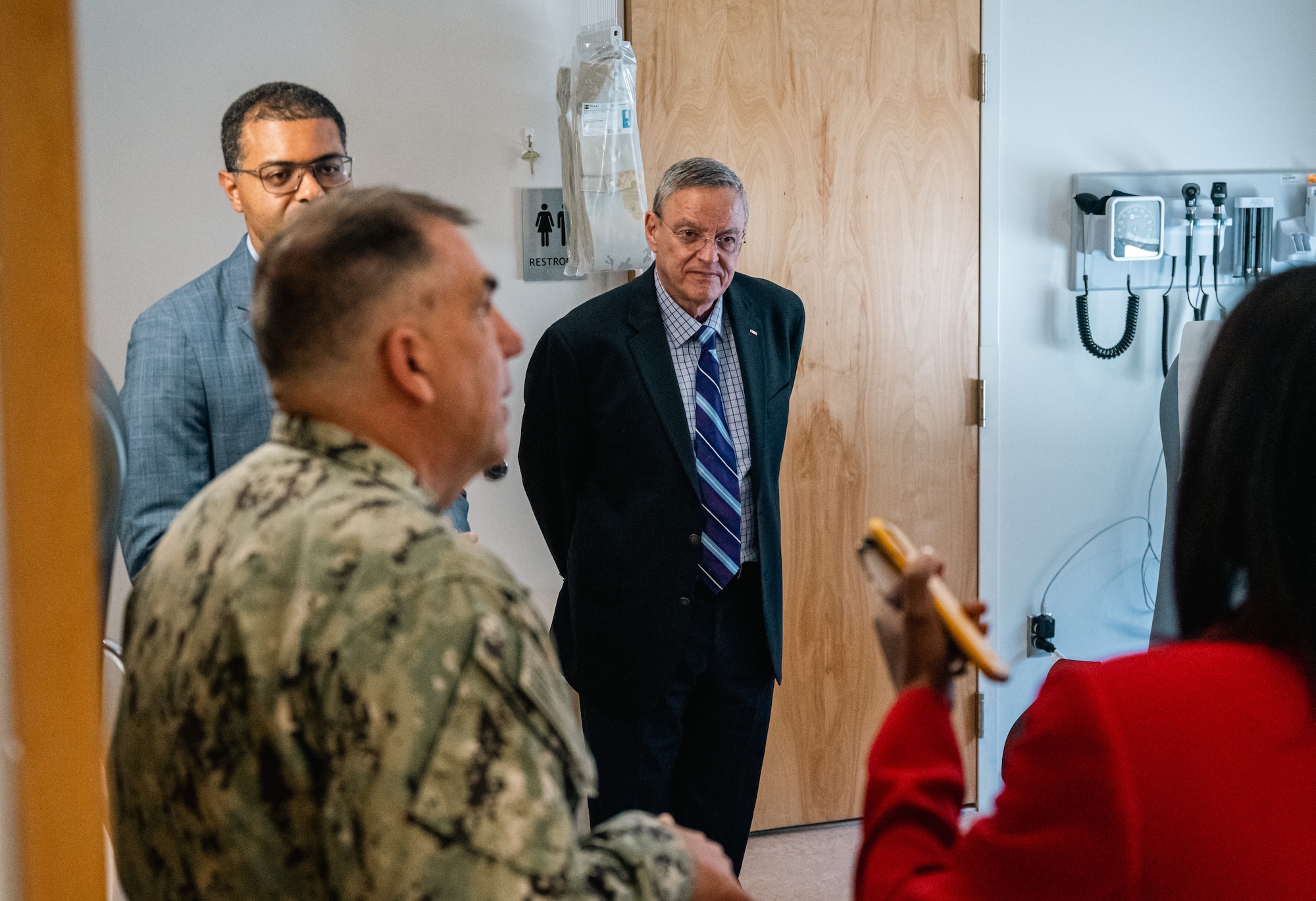 Two men in a suit and a navy man listen to a women in a red blazer