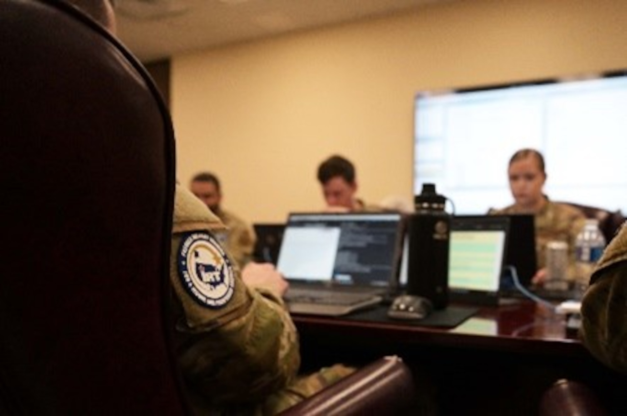 Photo of Airmen at a conference table working on computers.